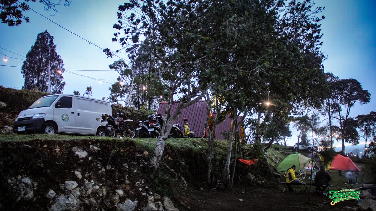 Suasana camping santai di perbukitan bersama, dikelilingi tenda, motor, dan cahaya yang hangat.